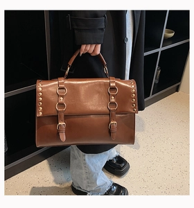 Detail of brown vintage satchel showing metallic rivets and decorative buckle straps