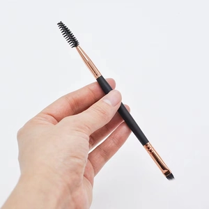 Dual-ended eyebrow brush with spiral spoolie and angled brush held against white background
