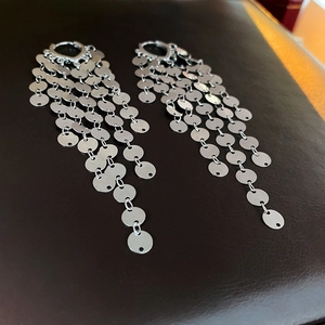 Detailed close-up of metallic silver sequin fringe drop earrings on leather surface