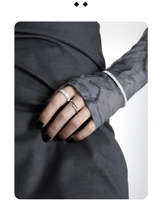 Close-up of minimalist silver rings and textured bracelet on grey fabric background