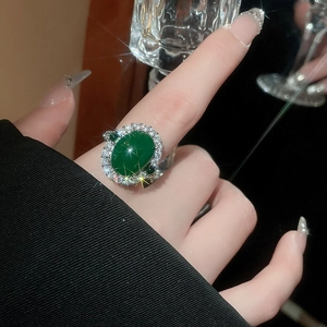 Gros plan d'une bague ovale vert émeraude sertie de zircons luxueux portée au doigt