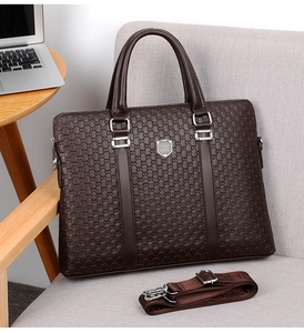 Close-up of textured dark brown leather briefcase with silver logo and shoulder strap