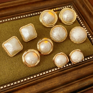 Macro detail of gold plated cotton pearl earrings displayed on green textured fabric