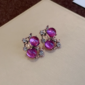 Macro shot of vintage purple berry stud earrings with antique gold leaves and crystals