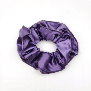 Detail view of purple satin scrunchie with dark purple stitched edges on white background