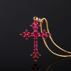 Macro shot of gold cross pendant with red crystals and box chain over black background
