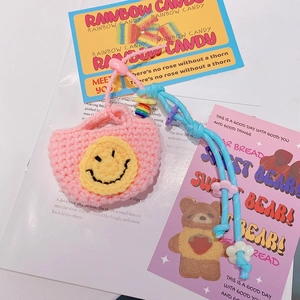 Gros plan d'un mini sac porte-clés rose tricoté avec smiley jaune et cordon bleu tressé