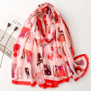 Pink scarf with cartoon cat prints and red edges displayed on a white table with a magazine