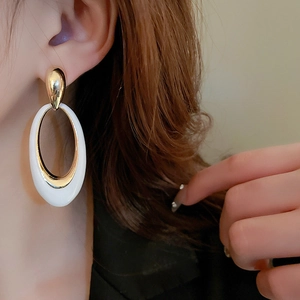 Detailed view of large oval drop earrings with white enamel finish and gold plating on model