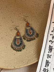 Détail de boucles d'oreilles bohèmes vintage avec gemmes oranges et glands perlés