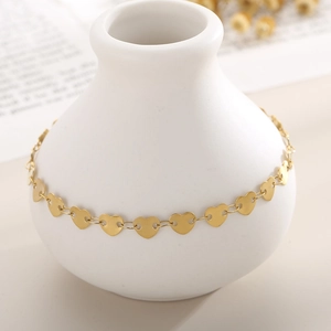 Detail of heart-shaped gold anklet wrapped around a white ceramic vase for elegant display