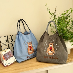 Detail of embroidered bear on nylon tote bags with drawstring closure in blue and grey
