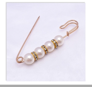 Detail of gold safety pin with four white pearls and crystal-encrusted spacers on fabric