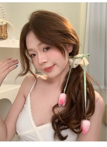 Close-up of a beige ribbon hair clip with pink tulip flower and green ribbons on hair
