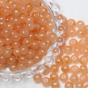 Close-up of 8mm orange glass beads with golden mesh patterns in a glass bowl