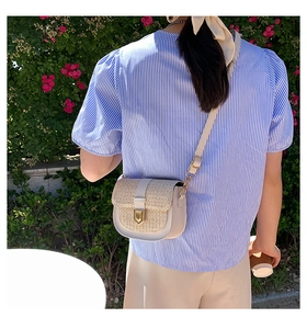 Close-up of a woven straw saddle bag with gold buckle on a woman in a garden