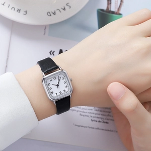 Close-up of a square silver quartz watch with black leather strap on a woman's wrist