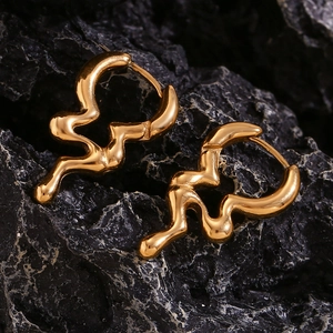 Macro shot of gold liquid irregular wavy hoop earrings on a black stone surface