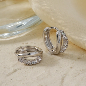 Close-up of silver U-shaped earrings with micro-paved white zircon stones on silk