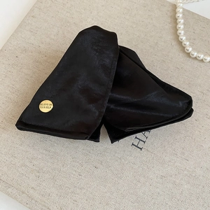 Detail of black satin fabric hair claw with a gold metal tag engraved 'Believe In Your Self'
