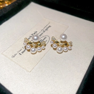 Close-up of elegant gold pearl earrings with zircon inlay on a beige display card
