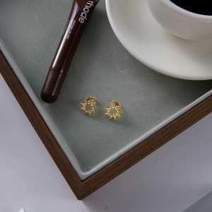 Macro detail of gold sun-shaped zircon earrings on a luxury velvet jewelry tray