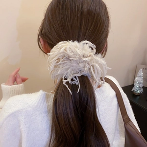 Détail d'un chouchou élégant en plumes blanc crème sur une queue de cheval de cheveux bruns