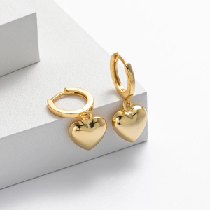 Detail view of golden heart drop earrings displayed on a minimalist white geometric stand