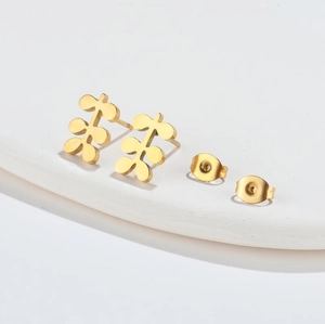 Minimalist gold stainless steel earrings with three round leaf motifs on a white tray