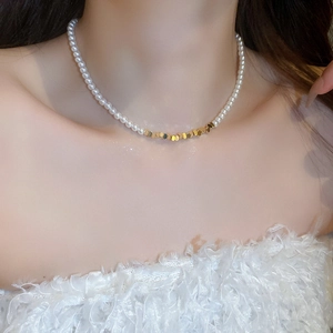 Detail shot of pearl choker with golden geometric charms on a model's neck