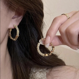 Detail of gold hoop earrings with metallic beads and pave-set zircons on a female model