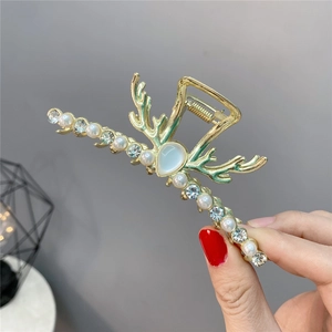 Dettaglio molletta per capelli a corno dorata con strass blu e perle nella mano