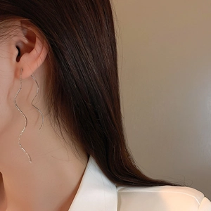 Detail of silver wavy drop earrings showing the elegant drape and textured finish on a model