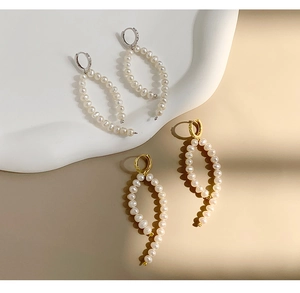 Detailed view of long Baroque pearl earrings in gold and silver finishes on a tray