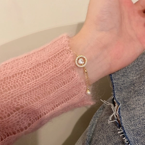 Detalle del colgante de corazón de cristal en cadena dorada con perlas en la muñeca