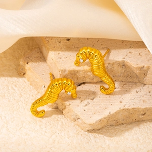 Detailed macro view of golden seahorse stud earrings with zircon eyes on silk background