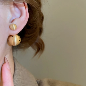 Detail of 18k gold-plated matte double ball earrings with black polka dots on ear