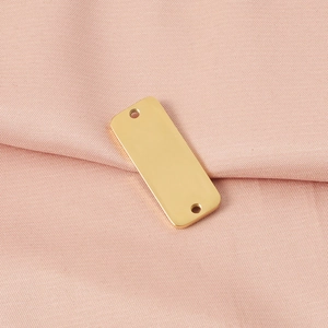 Close-up of golden rectangular stainless steel pendant tag on soft pink fabric background