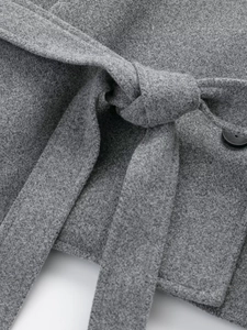 Close-up of gray wool coat detailing the thick fabric texture, waist belt and black button