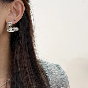 Minimalist silver heart earrings on model with polished 3D hollow metal design