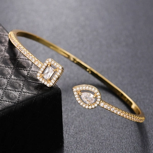 Detail view of gold open cuff bracelet with square and teardrop zircon stones on gift box