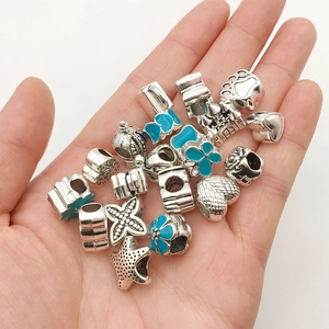 Close-up of DIY silver charms and beads with blue enamel designs held in hand