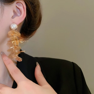 Detail of gold layered tassel earrings with ginkgo leaves and a glossy white pearl stud