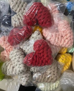 Close-up of bulk heart-shaped hand-knitted pillows in assorted colors with polybag packaging
