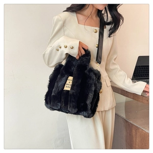 Detail of black faux fur tote bag with broad shoulder strap and woven slogan tag