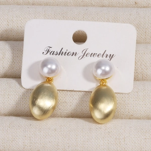 Elegant gold pearl earrings with brushed metal finish shown on a jewelry display
