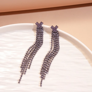 Close-up of geometric purple tassel earrings with rhinestones on a ceramic tray