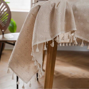 Macro detail of beige linen tablecloth with red floral patterns and hanging tassels