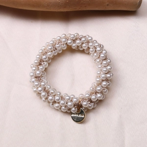 Close-up of woven pearl hair scrunchie with a round gold Morave brand metal charm
