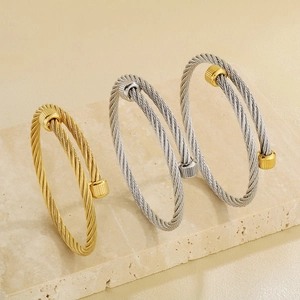 Three twisted cable stainless steel bangles in gold, silver, and two-tone on stone